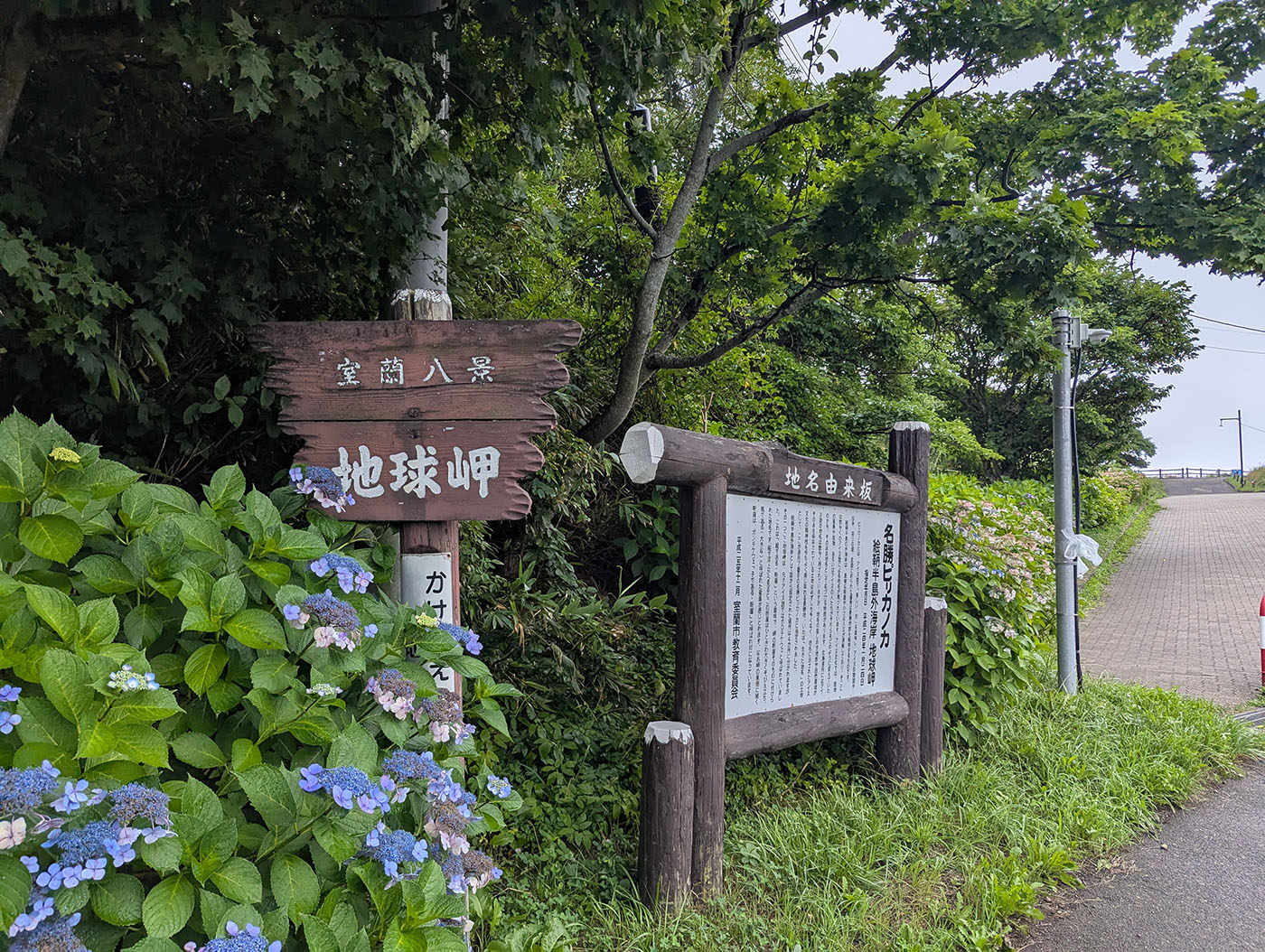 地球岬の入口に立つ木製の案内板と由来板