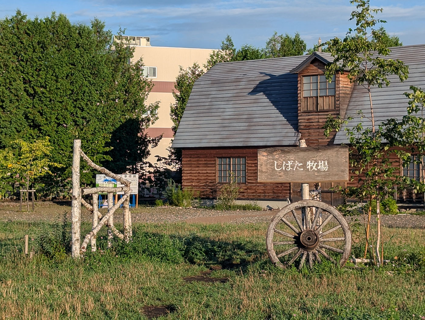 道の駅おとふけ「なつぞらのふる里」にある「しばた牧場」の入口。木製の案内板と古い車輪、木造の牛舎が背景に見える。