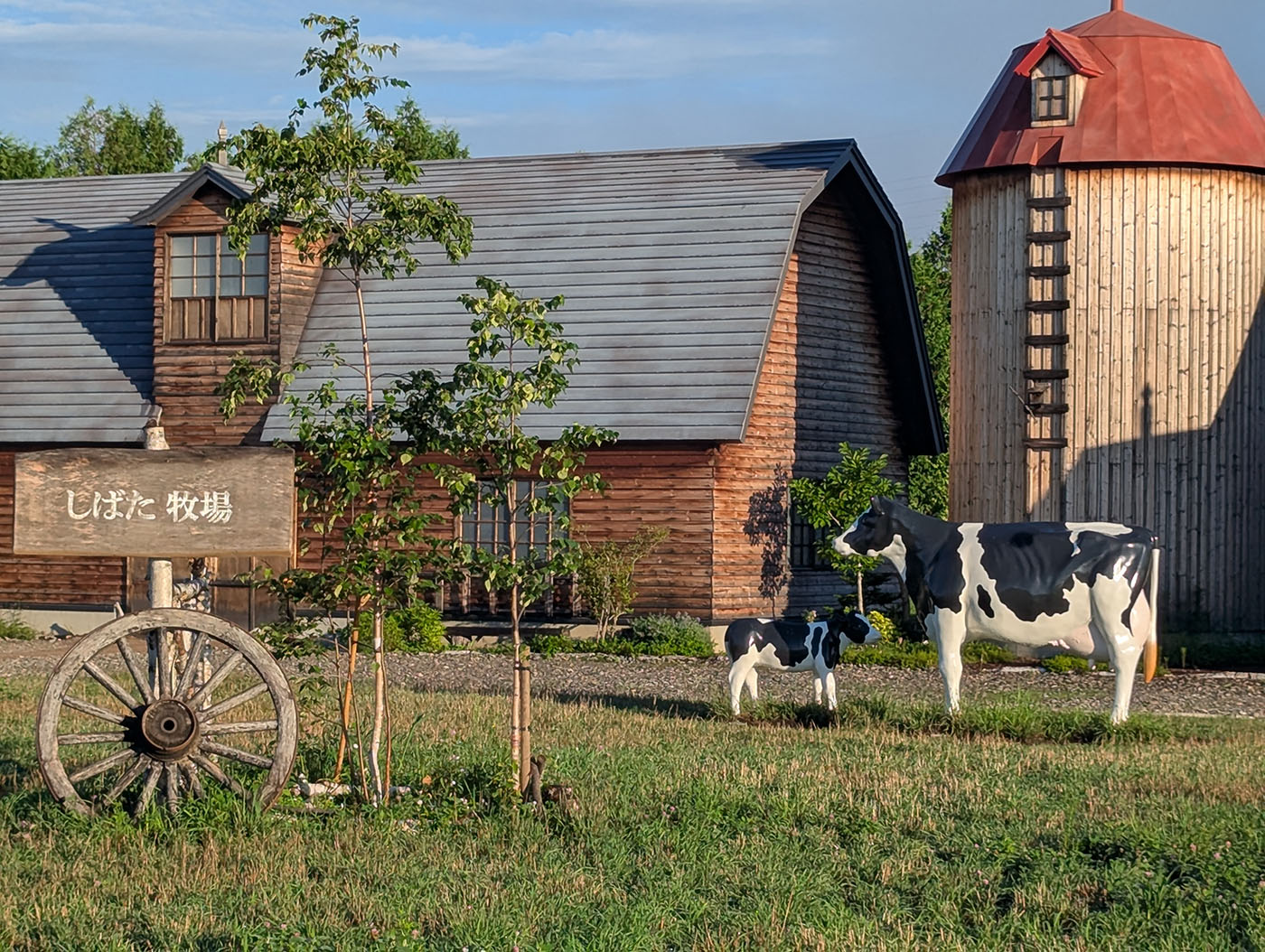 道の駅おとふけ「なつぞらのふる里」にある「しばた牧場」のフォトスポット。木造の牛舎とサイロの前に、親子の乳牛模型が立っている。