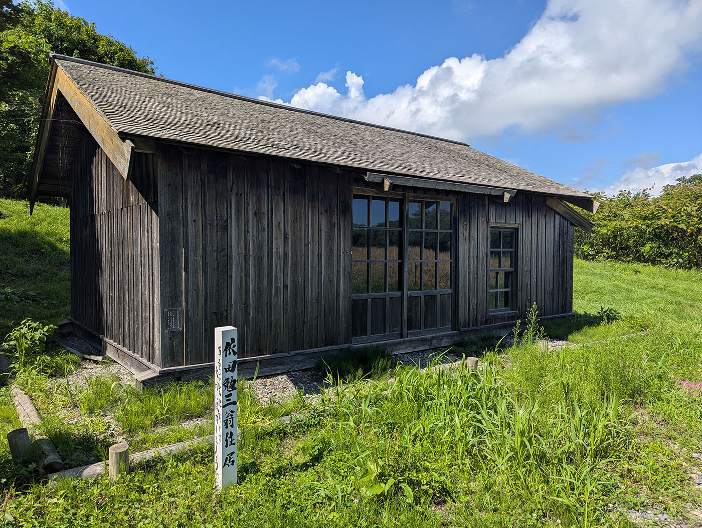 晩成社跡地に残る依田勉三住居の復元建物。木造の質素な小屋が青空の下に佇んでいる。