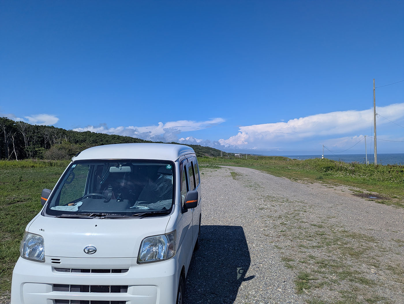 北海道・晩成海岸近くの青空と海を背景に、道端に停車する白いハイゼットカーゴ。真夏でも爽やかな景色
