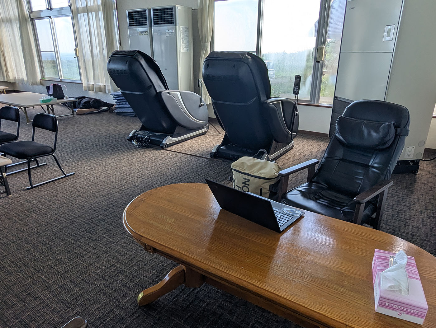 晩成温泉の休憩所。マッサージチェアやソファが並び、窓際には海を望みながらくつろげる空間が広がっている。テーブルにはノートPCが置かれ、作業も可能。