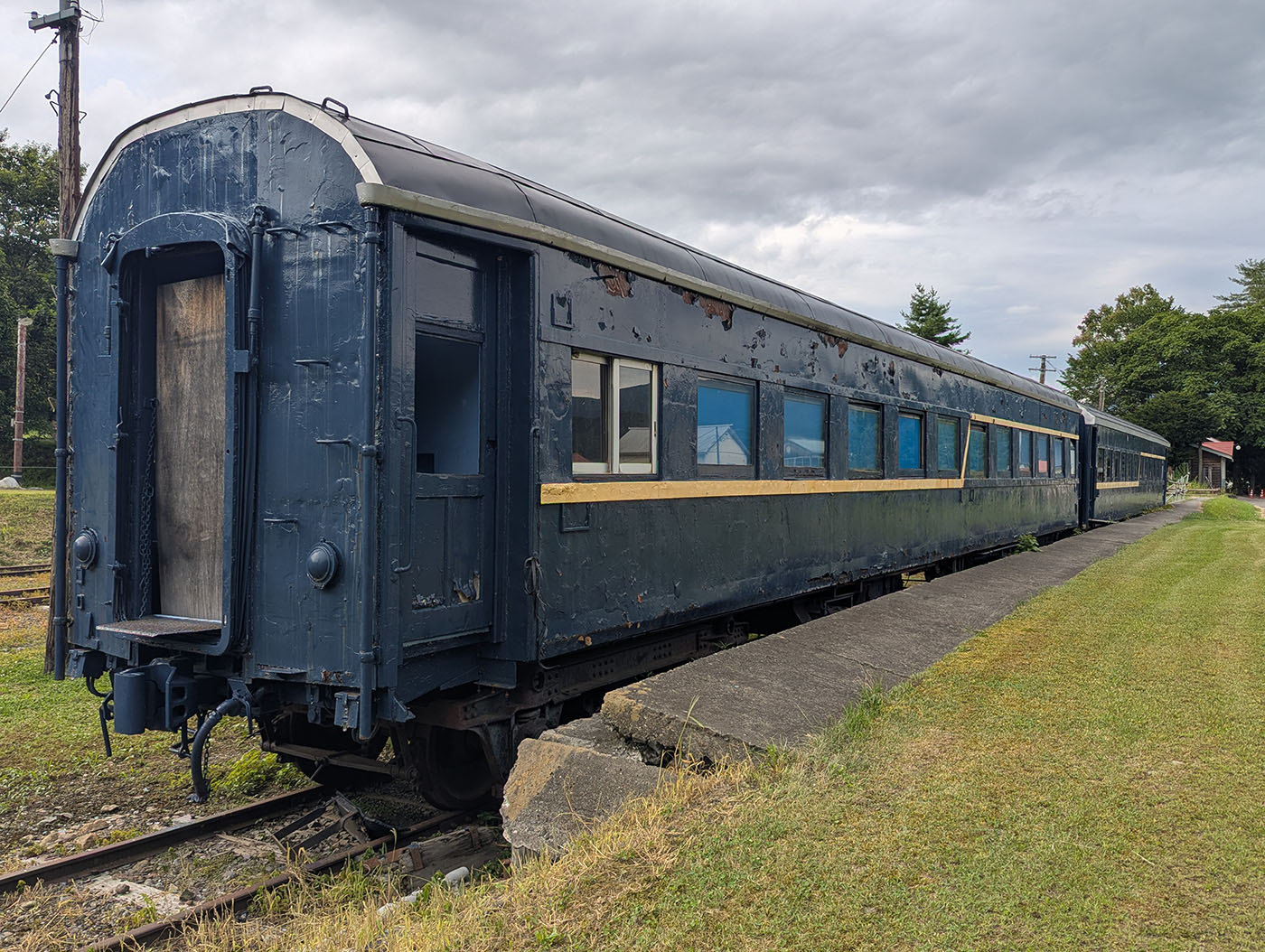 青い塗装が剥がれ、経年劣化の跡が残る古い客車。窓には青みがかったガラスが並び、側面にはかつての黄色いラインがかすかに残っている。