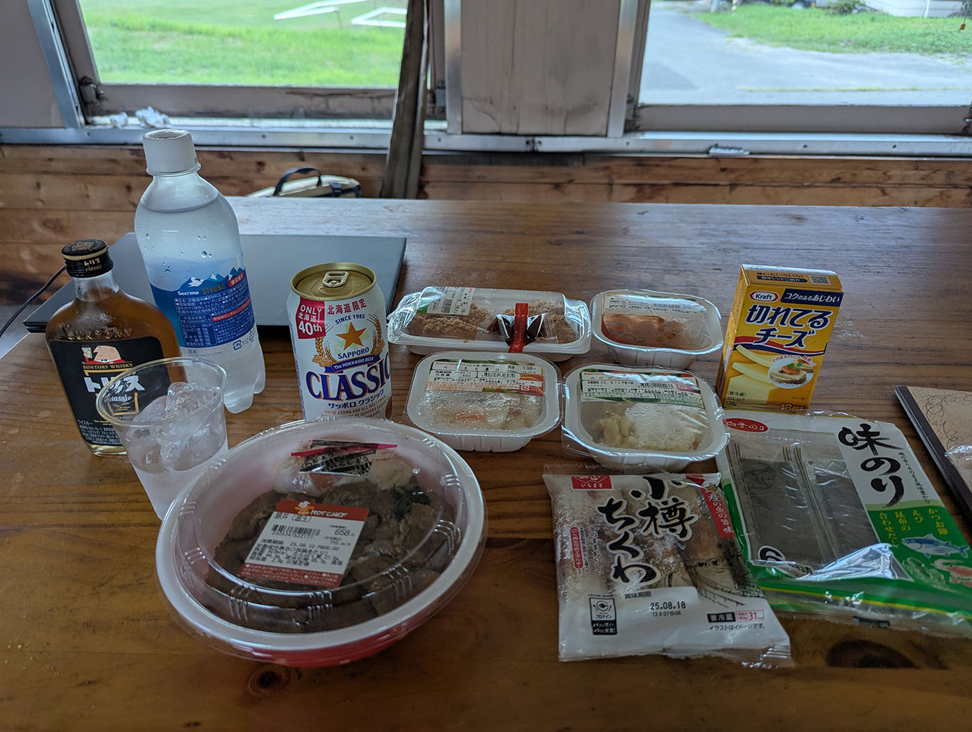 車両内のテーブルに並ぶ晩酌セット。トリスウイスキー、サッポロクラシック、総菜やおつまみがずらりと並ぶ。