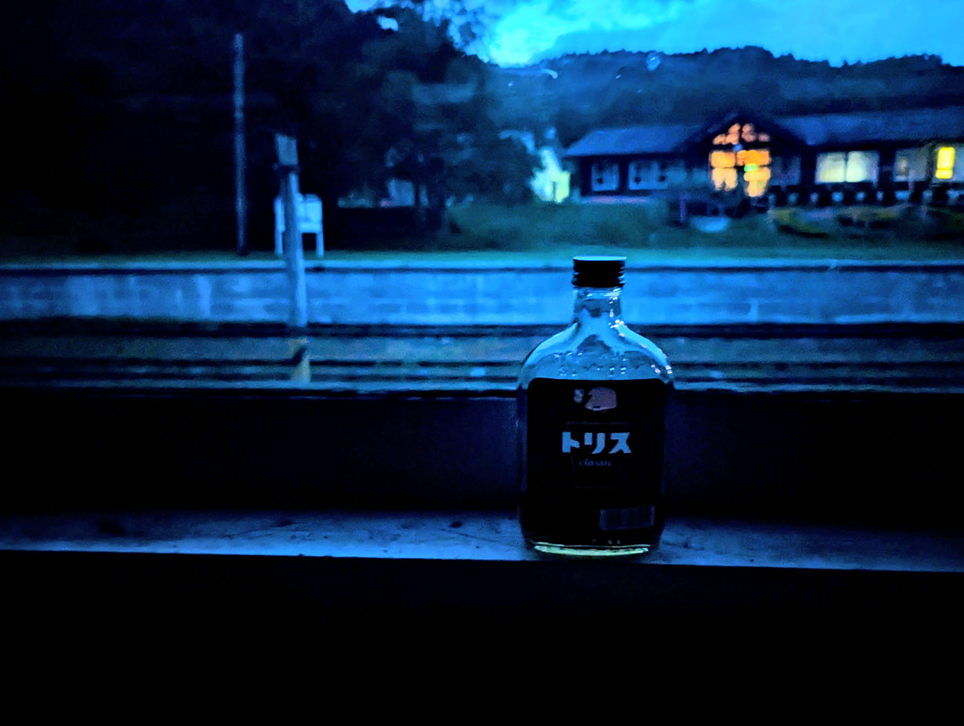 北海道むかわ町の富内銀河ステーションの夜景。廃線ホームの車両窓辺に置かれたウイスキー「トリス」の瓶と、灯りがともる駅舎が幻想的に映る。