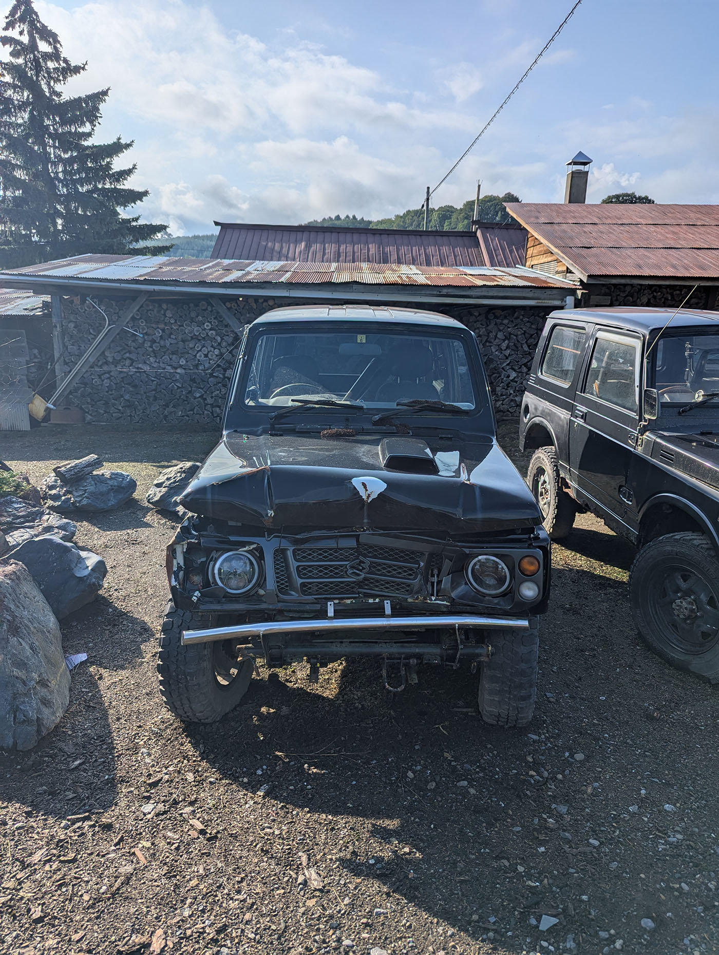 岩場の前に停まる黒いジムニー。ボンネットが大きく凹み、フロント周りに損傷が見られる。