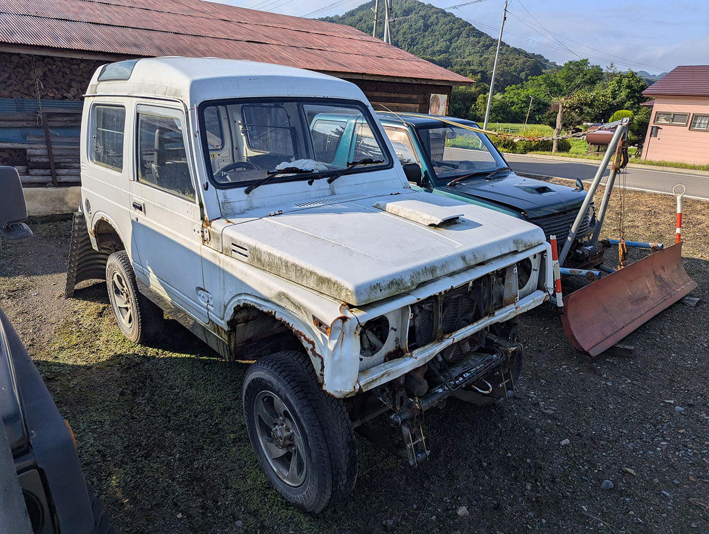 錆と苔が混じるボディの白ジムニー。横からの姿に歴戦の跡が刻まれている。