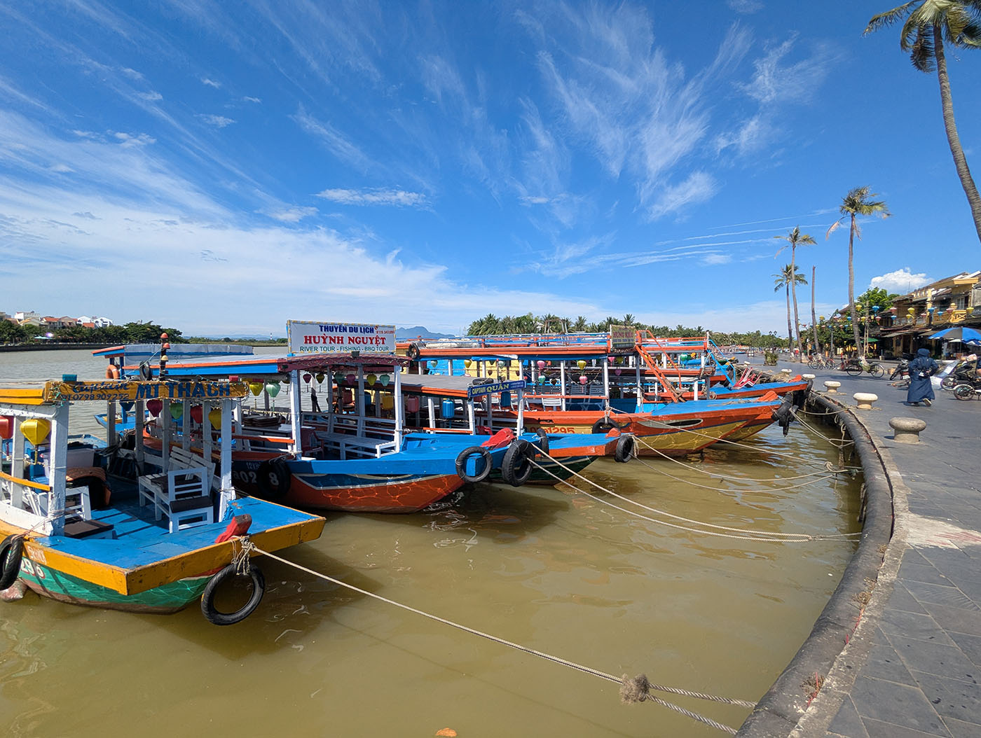 ホイアンの川辺に並ぶカラフルな遊覧船。青空と水辺が広がり、港町として栄えた面影を残している。