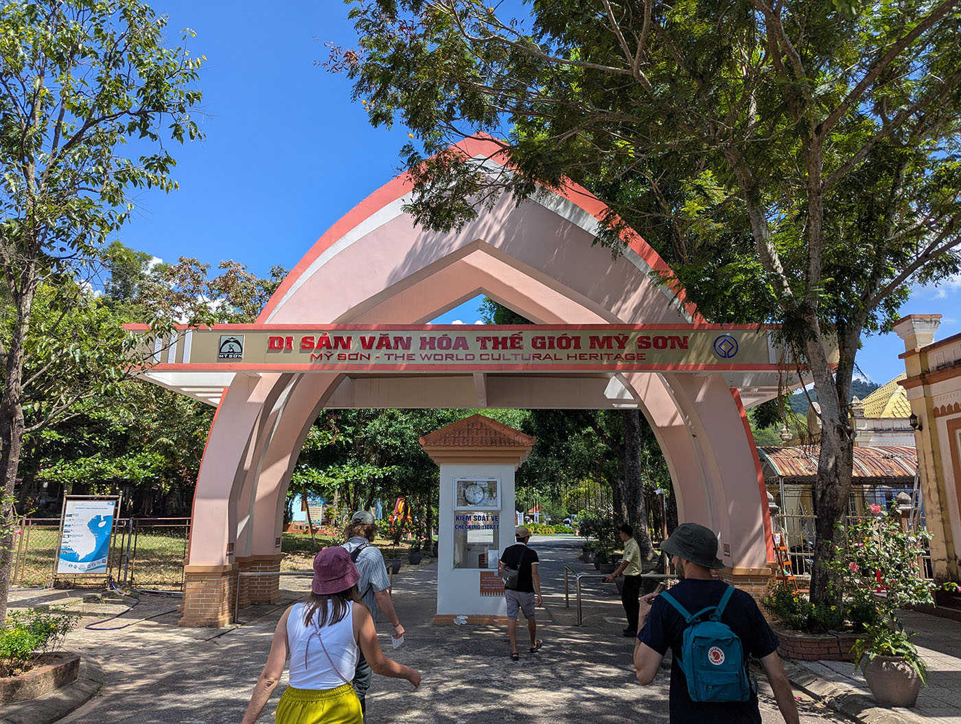 ミーソン遺跡の入口ゲート。赤いアーチに“MY SON - THE WORLD CULTURAL HERITAGE”と記された看板が掲げられ、多くの観光客が中へ向かって歩いている