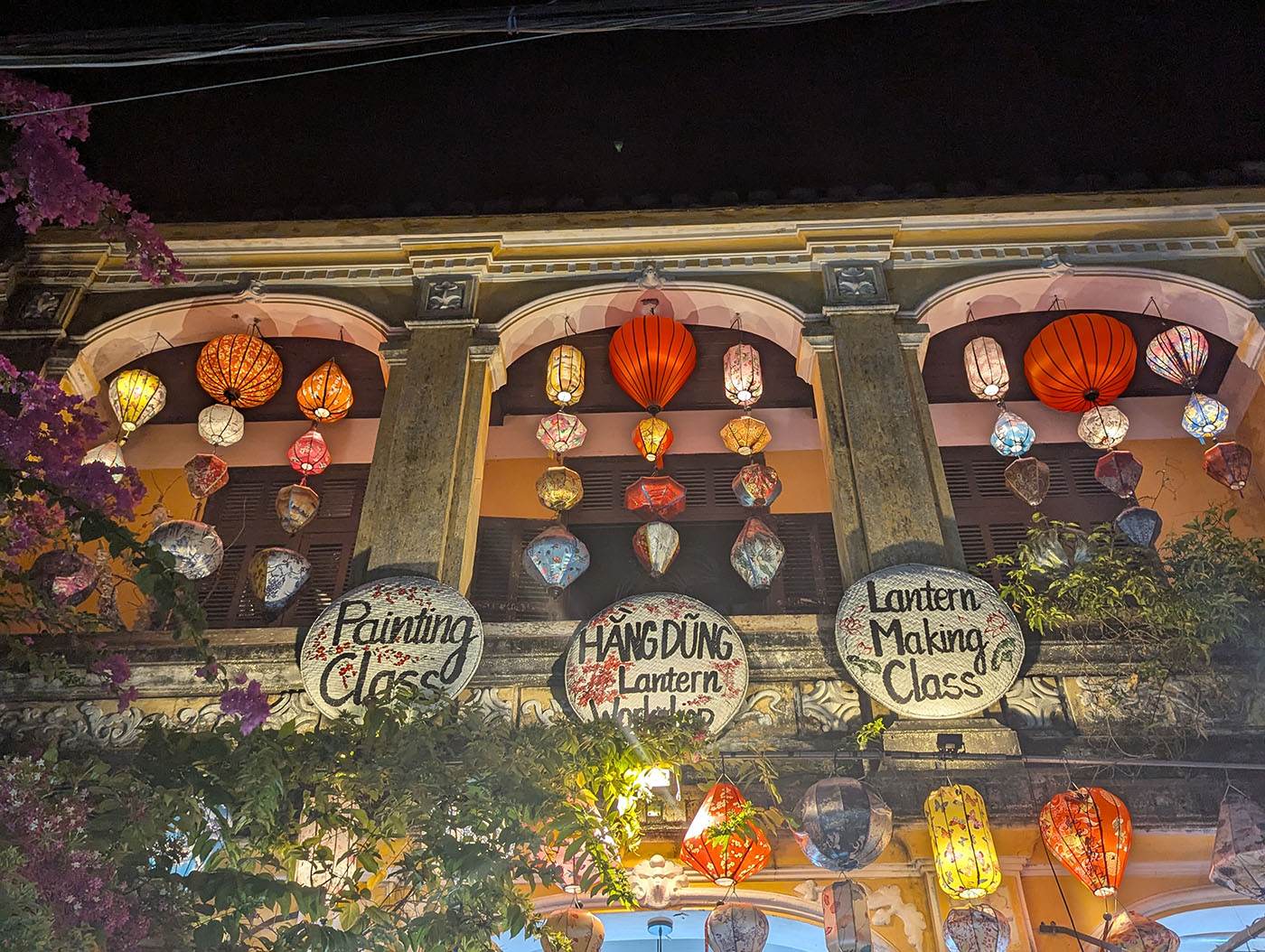 ホイアン旧市街の二階建て建物に吊るされたカラフルなランタンと、ランタン作りやペインティングの看板