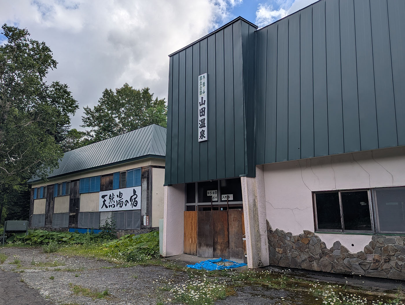 「天然湯の宿」と書かれた看板とともに、老朽化が進んだ外観。かつての賑わいを思わせる佇まいが残る。