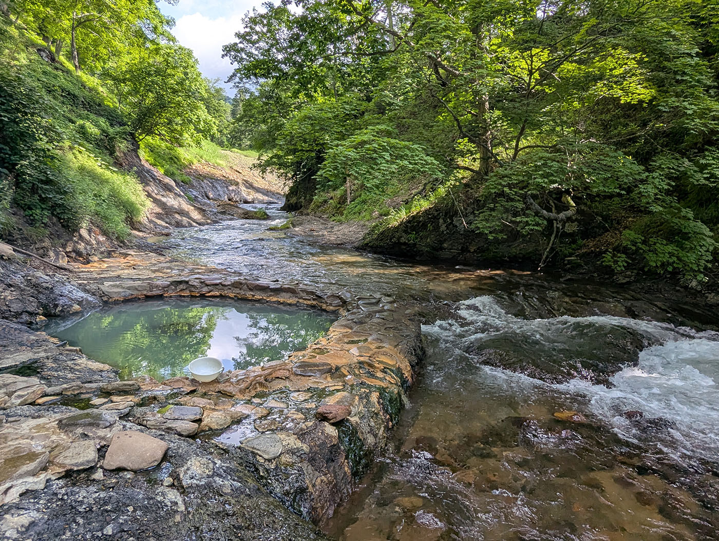 鹿の湯温泉とユウヤンベツ川の風景。石造りの湯船が川沿いに設けられ、自然と調和した絶景の野湯。