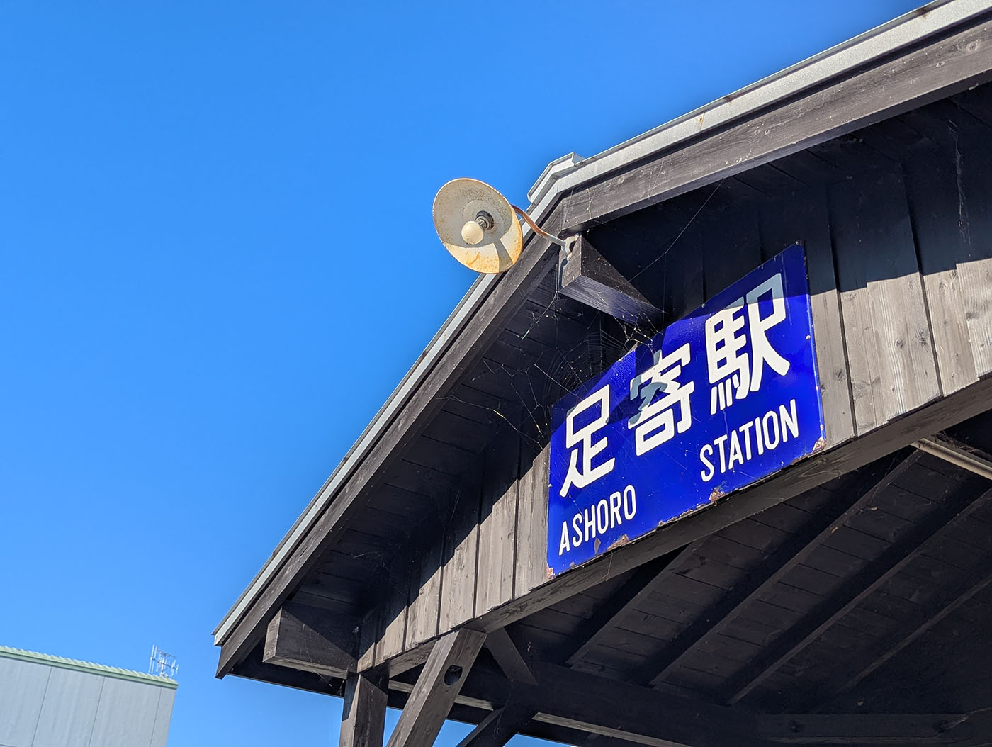 澄み切った青空の下、旧足寄駅舎に掲げられた「足寄駅 ASHORO STATION」の青い駅名看板とレトロなスピーカー。