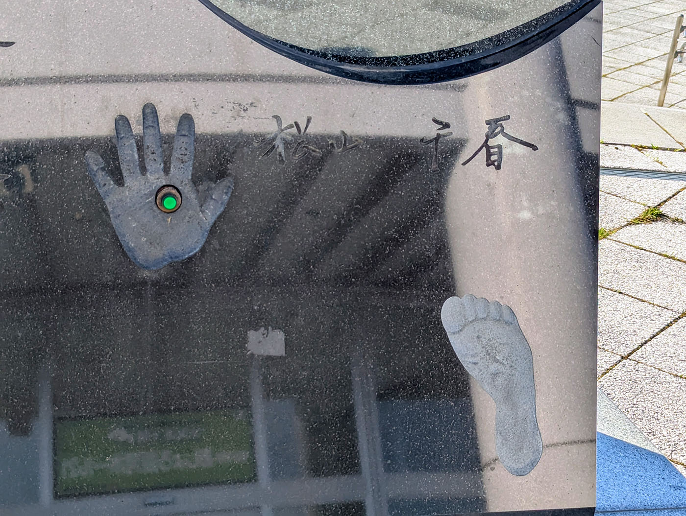 道の駅あしょろ銀河ホール21にある松山千春さんの手形と足形のモニュメント。黒い石板に左手と右足の型が刻まれ、手形中央には緑色のボタンが埋め込まれている。