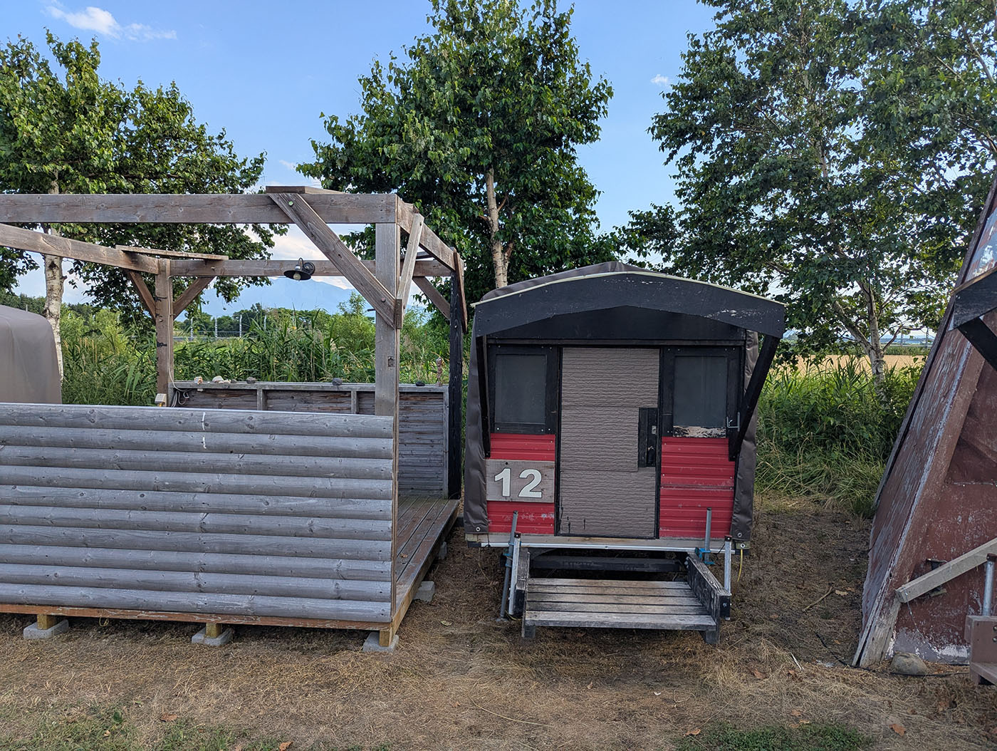 クリオネキャンプ場のモバイルハウス12番の外観。木製のデッキと屋根付きのスペースが備えられている。