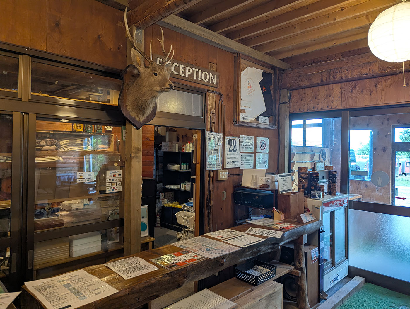 クリオネキャンプ場の受付カウンター。ログハウス風の管理棟には鹿の剥製が飾られ、壁には注意書きやTシャツが掲示されている。