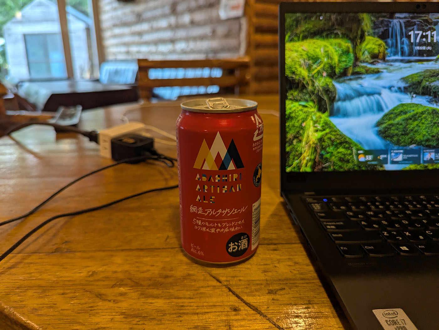 クリオネキャンプ場のログテーブルに置かれた網走クラフトビール「網走アルチザンエール」とノートパソコン。ノマドワークとご当地ビールの組み合わせが映えるワンシーン。