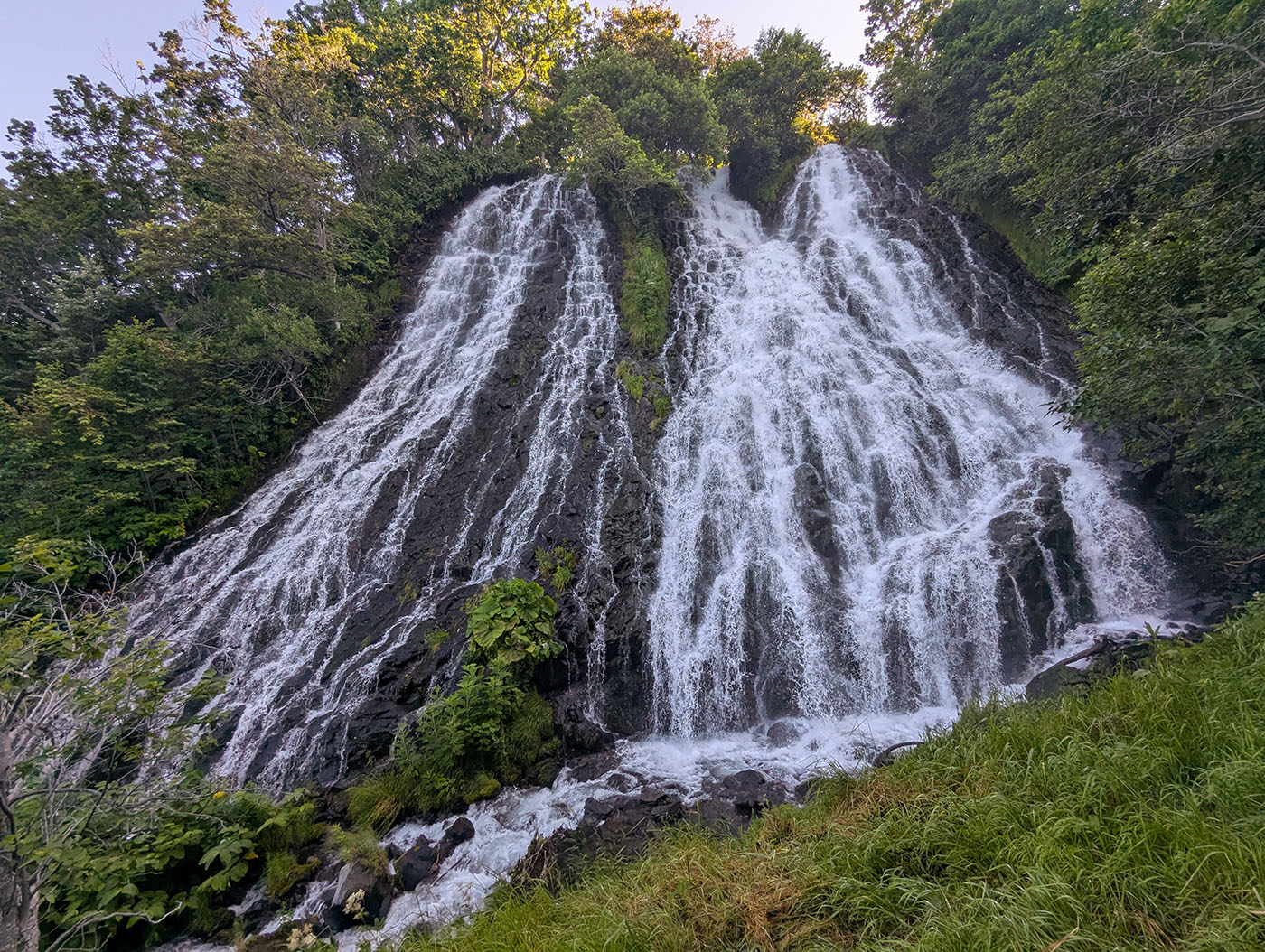 夏の朝日を背に、岩肌を白糸のように流れ落ちるオシンコシンの滝の全景。
