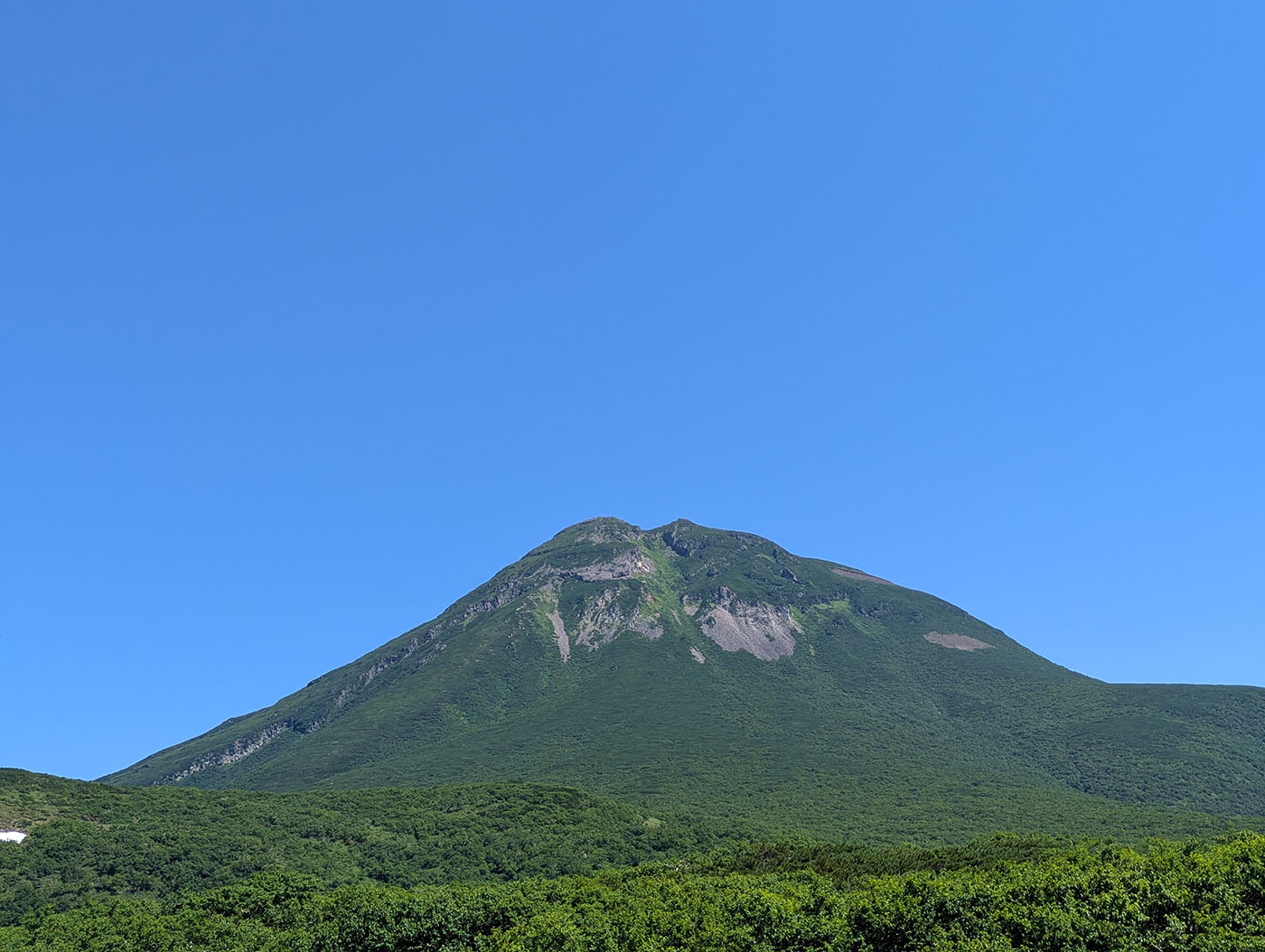 知床峠から望む羅臼岳。青空の下、緑豊かな斜面と岩肌がくっきりと浮かび上がっている。