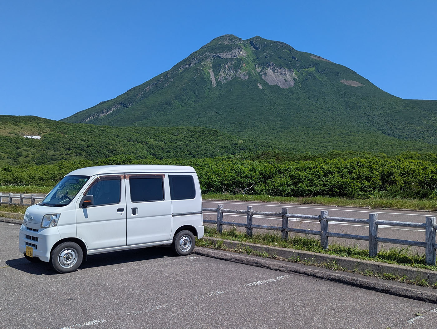 知床峠の駐車場に停めた白い軽バンと、その背後にそびえる夏の羅臼岳。