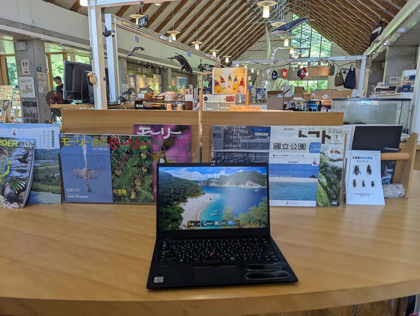 知床羅臼ビジターセンター館内のテーブルでノマドワーク。雑誌やパンフレットが並ぶ中、ノートパソコンを広げて作業している。