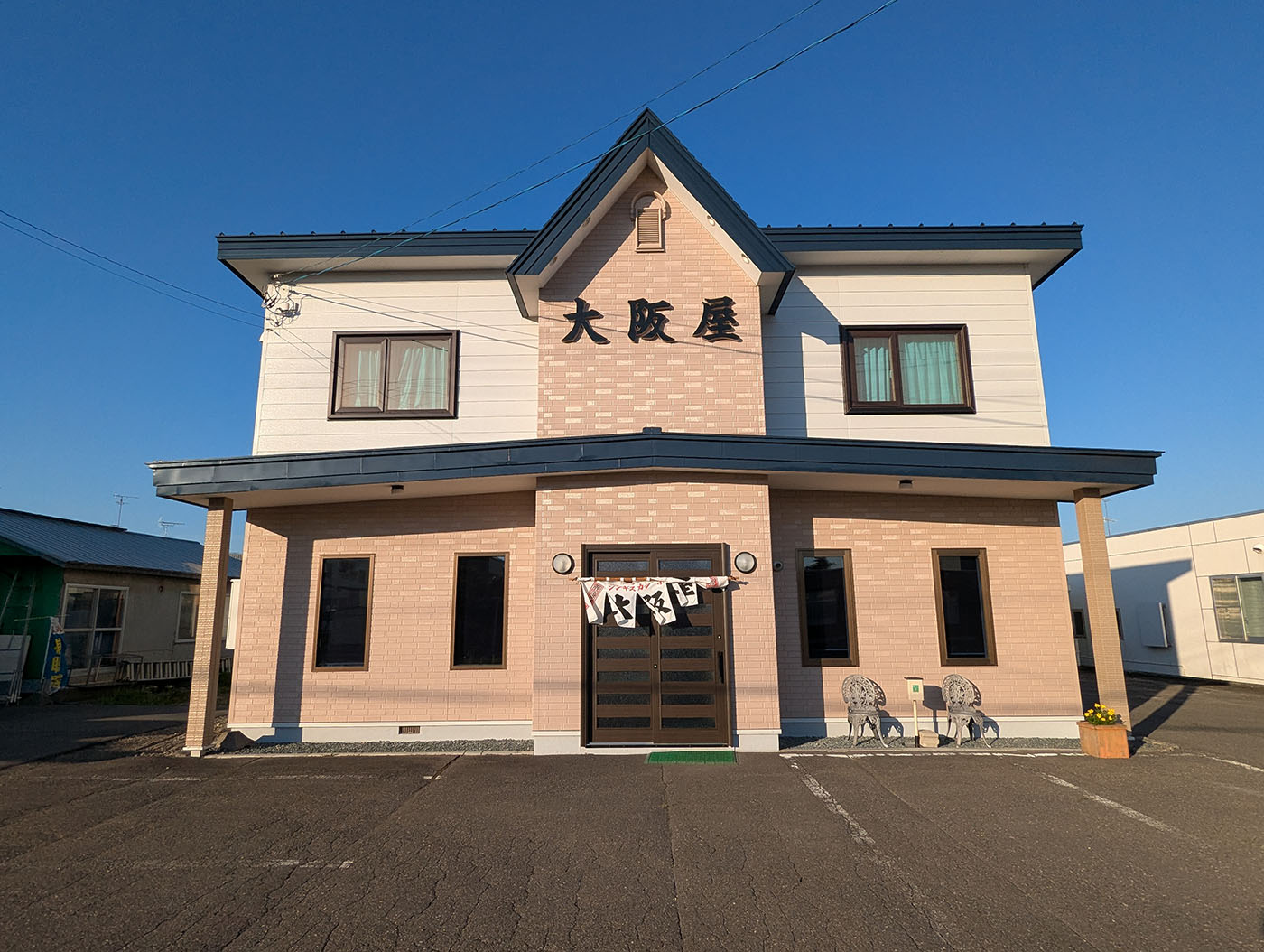 北海道鹿追町にある食堂「大阪屋」の店舗外観。青空の下、白とレンガ色のツートンの建物に「大阪屋」の看板が掲げられ、入り口には暖簾がかかっている。