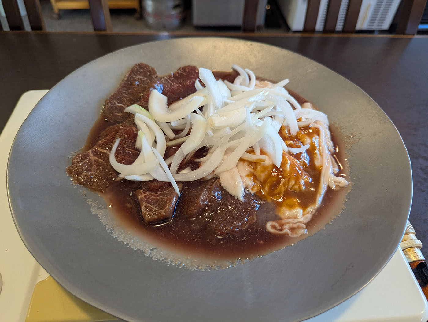 鹿追町「大阪屋」の名物ジンギスカン。金属製の皿に盛られた生の羊肉と玉ねぎが、特製の甘辛いタレにたっぷりと浸されて