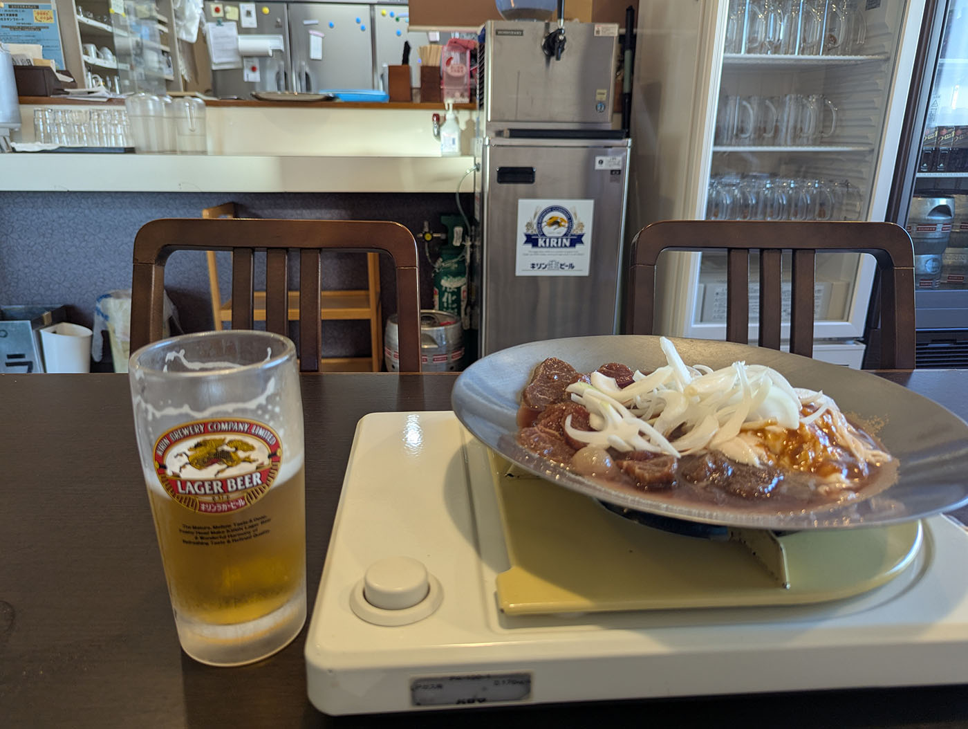 鹿追町の食堂「大阪屋」の店内で撮影された一枚。鉄板の上には玉ねぎとタレに漬け込まれたジンギスカン肉、横にはキリンラガービールのジョッキが置かれている。