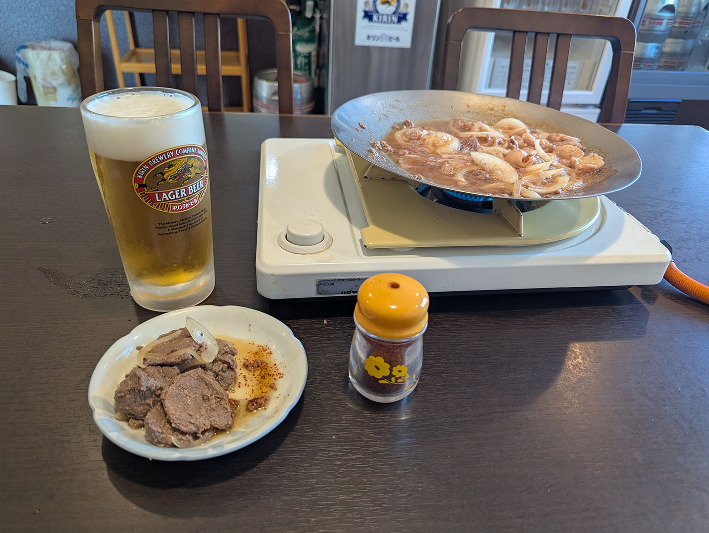 鹿追町「大阪屋」でのジンギスカン風景。鉄板で煮込まれる肉と玉ねぎ、生ビールのジョッキ、小皿の肉、黄色いフタの一味ボトルが並ぶテーブル。