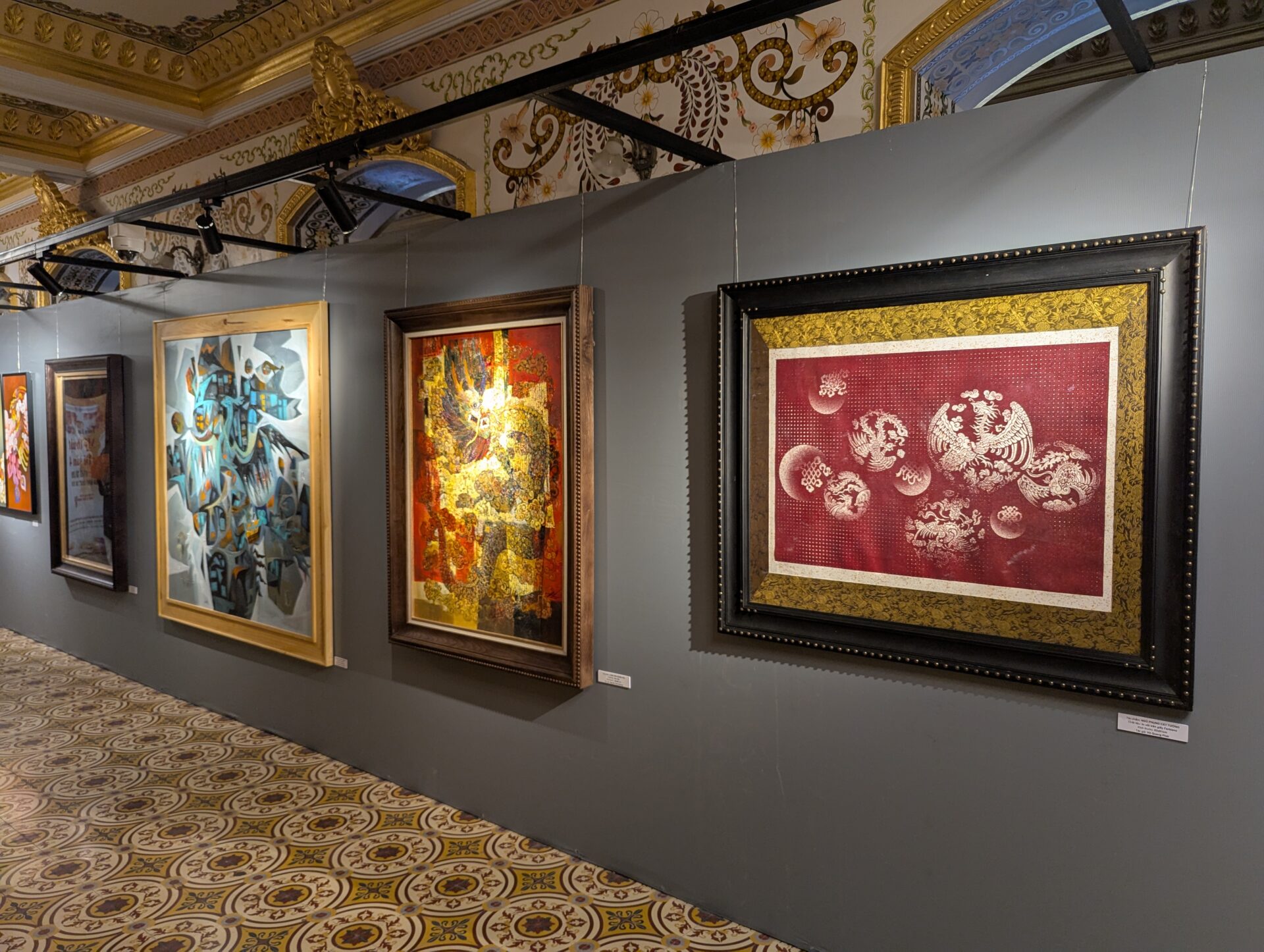 灰色の展示壁に沿って、抽象画や金箔を使った伝統絵画、赤地に白の龍や鳳凰を描いた作品など、多様なアート作品が並ぶ美術展会場。