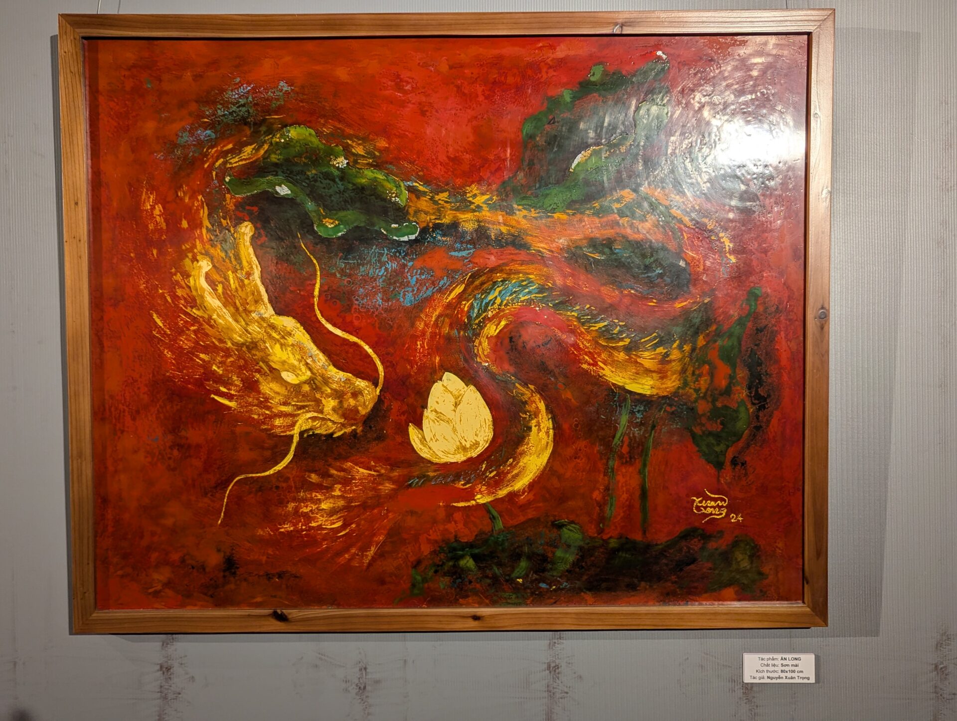 赤を基調に、黄色い龍と緑の龍が中央の蓮の花を囲むように描かれた抽象的な絵画。力強い筆致と鮮やかな色彩が印象的。