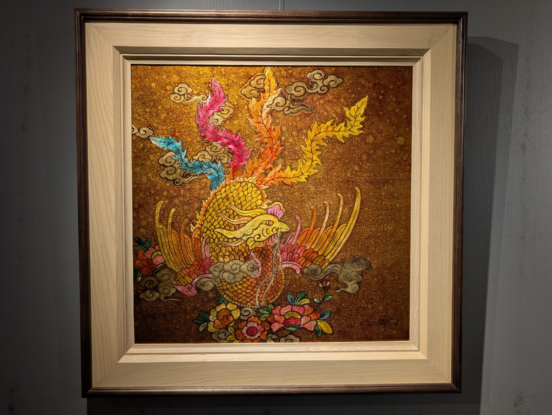 金色を基調に、色鮮やかな羽根と尾を持つ鳳凰を描いた絵画。背景には雲と花が配され、華やかさと神秘性を兼ね備えている。