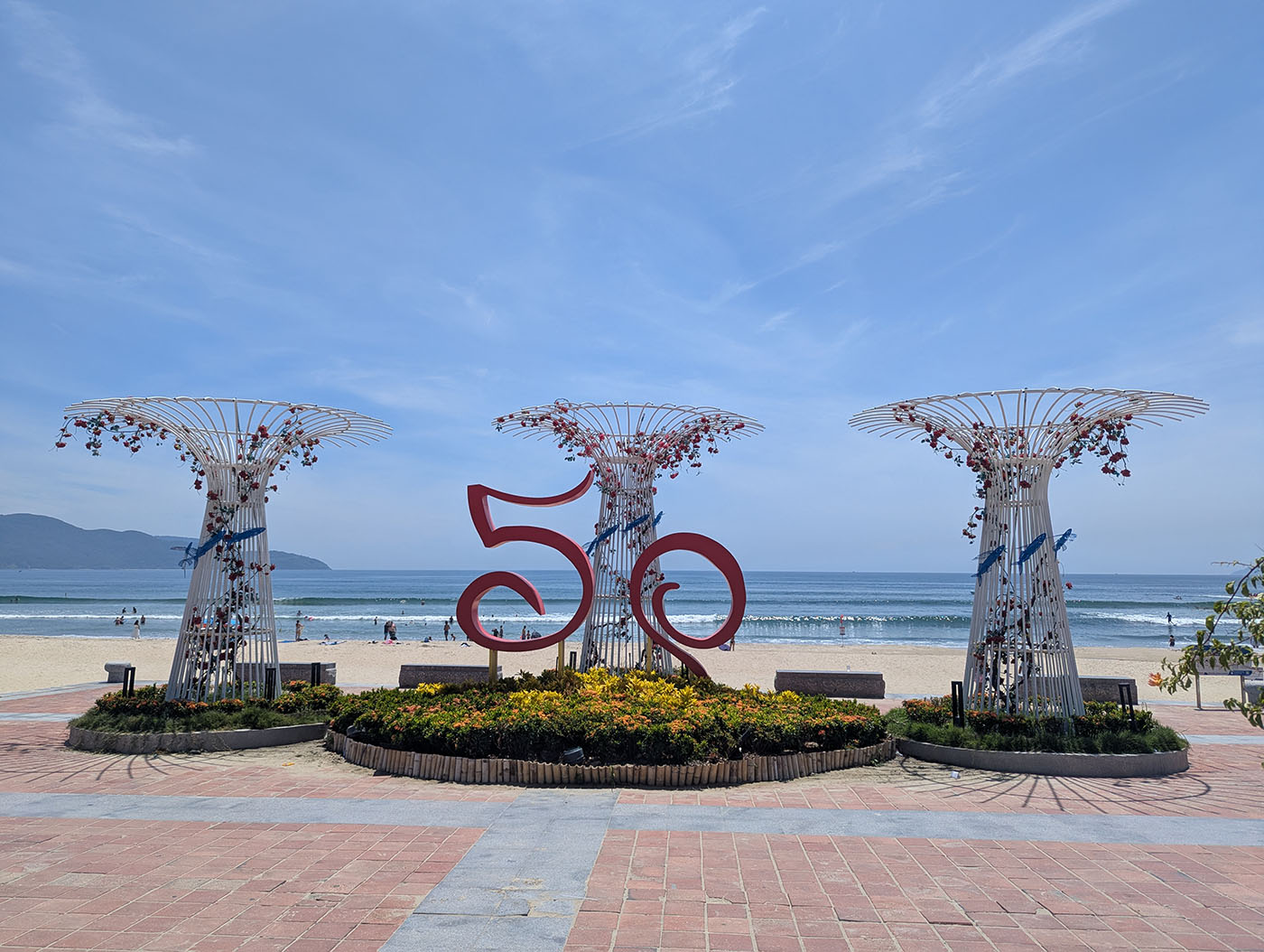 青空の下、ミーケビーチの入口に設置された「50」の赤いモニュメントと3本の装飾柱