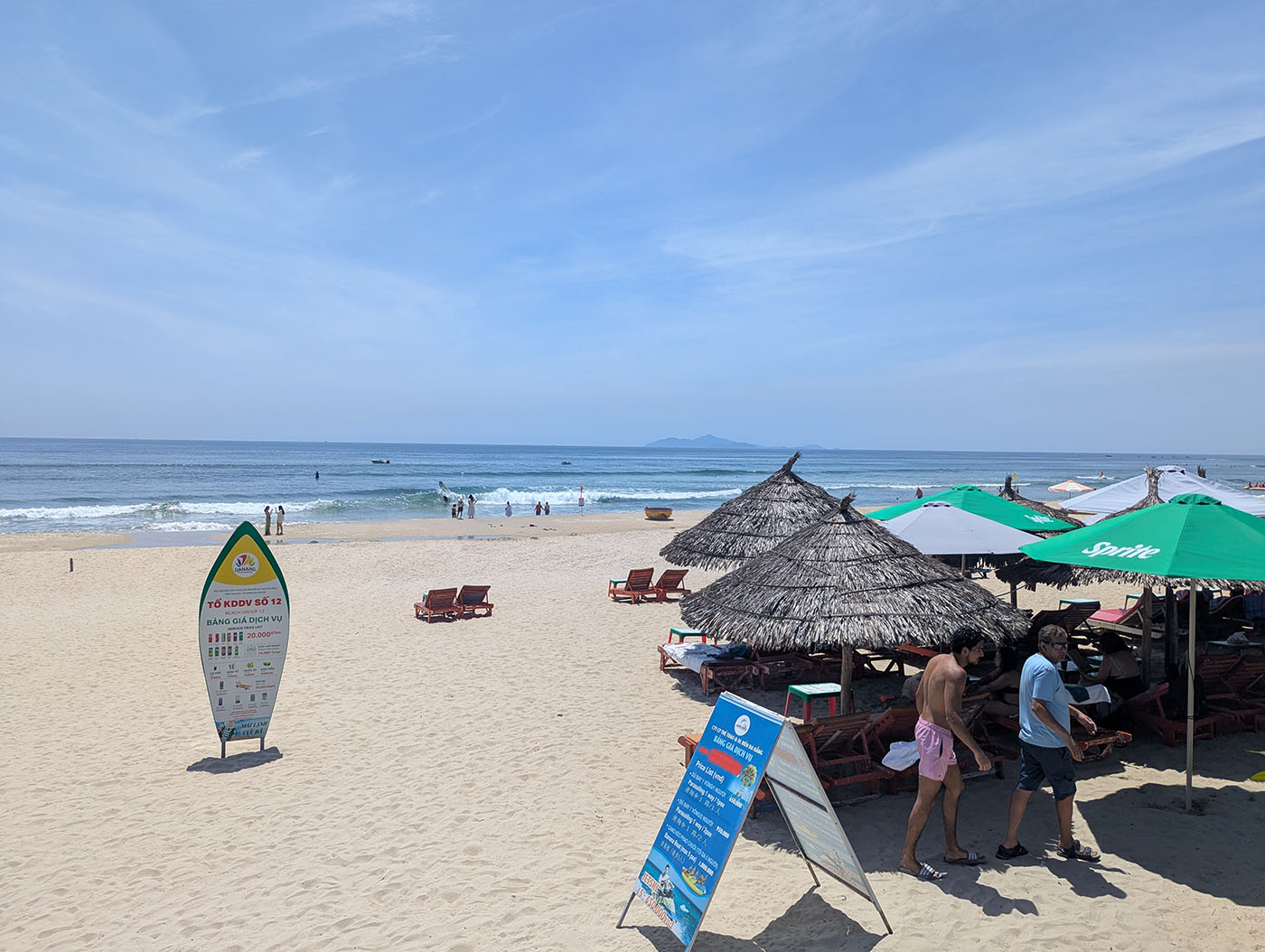 砂浜に並ぶパラソルとデッキチェア、奥には波打ち際で遊ぶ人々