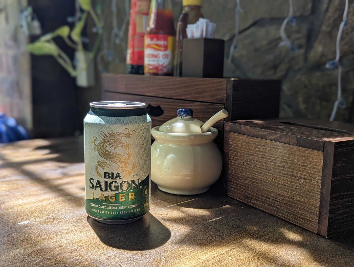 木のテーブルの上に置かれたBIA SAIGONの缶ビールと調味料類