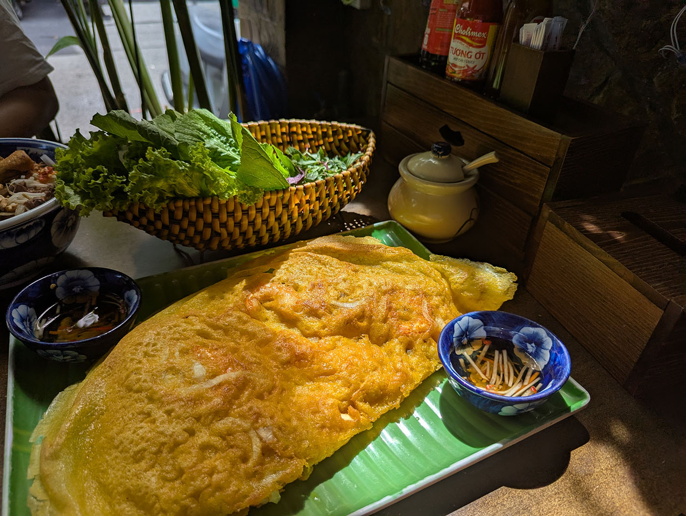 大皿に盛られた黄色いバイン・セオと、横に添えられたハーブと野菜の盛り合わせ