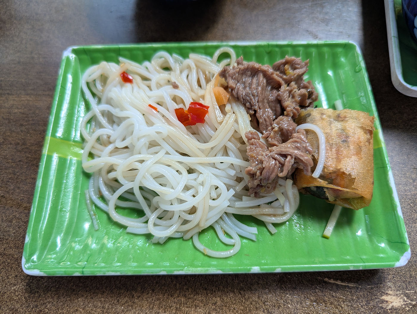 緑のプレートに盛られたフォーと牛肉、春巻きの取り分け皿