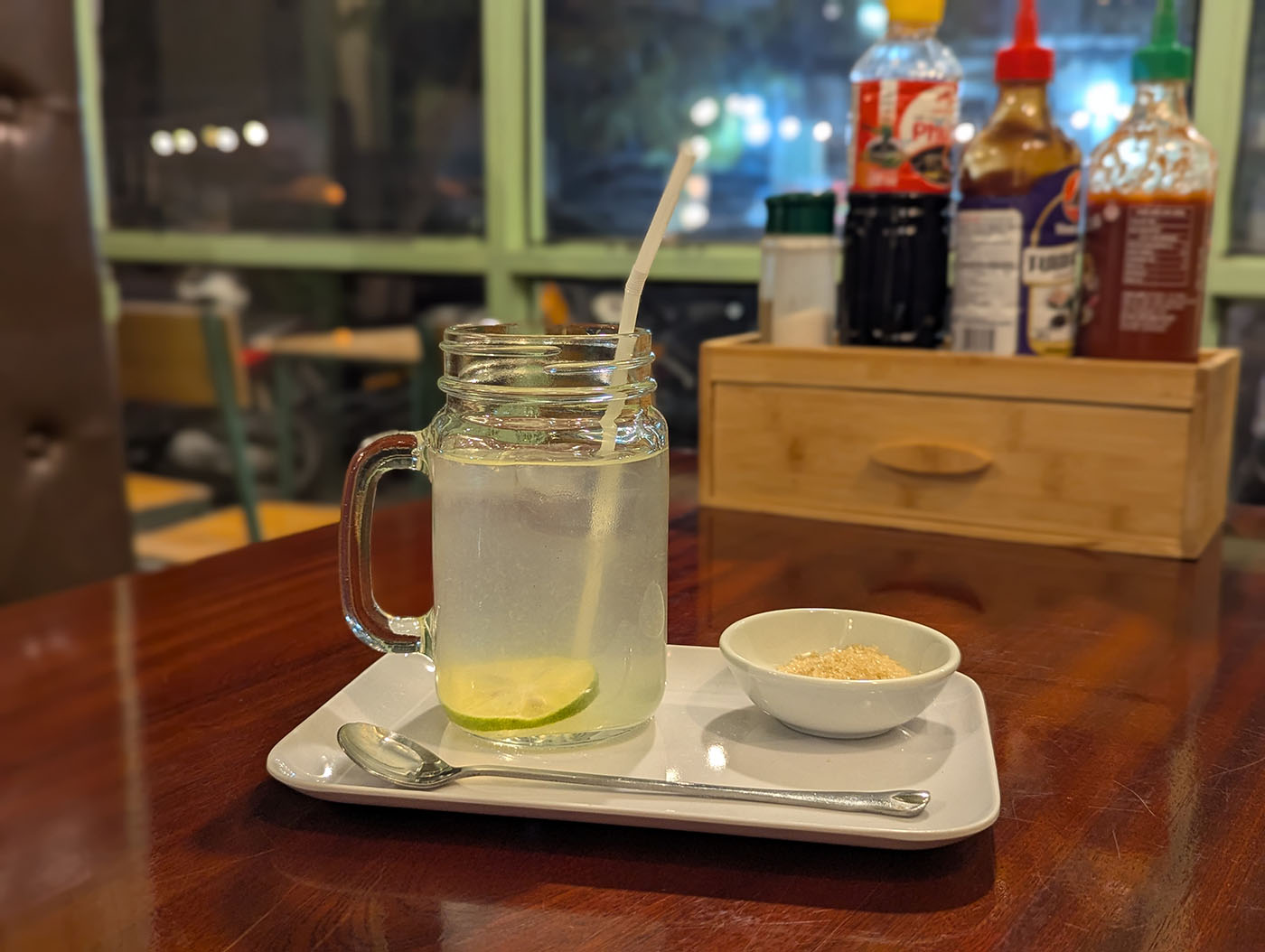 ライムが浮かんだソーダと砂糖の小皿、奥には調味料の瓶が並ぶテーブル