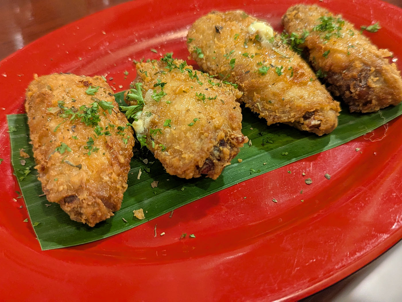 赤い皿に並べられた4つのフライドチキン。緑の葉の上に盛られている