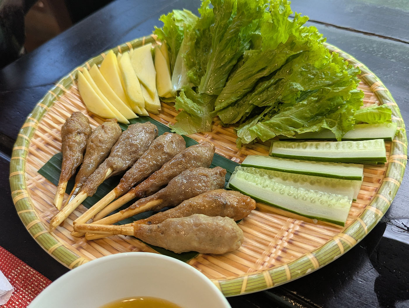 ベトナム料理の前菜プレート。串に巻き付けられた肉団子、レタス、きゅうり、マンゴーの薄切りが竹皿に美しく並んでいる。