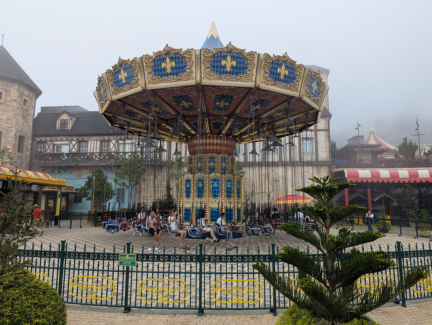 山頂の遊園地に設置されたチェーンスイング型の回転ブランコ。霧に包まれた幻想的な雰囲気の中、観光客が順番を待っている。