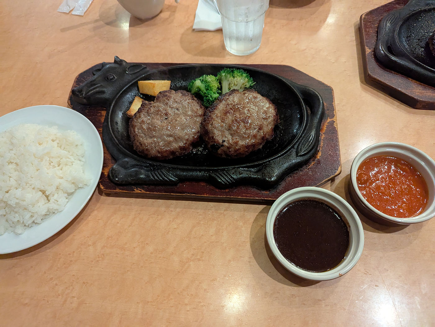 フォルクスのハンバーグダブルセット。鉄板の上で肉汁が弾け、ライスと2種のソースが添えられている。