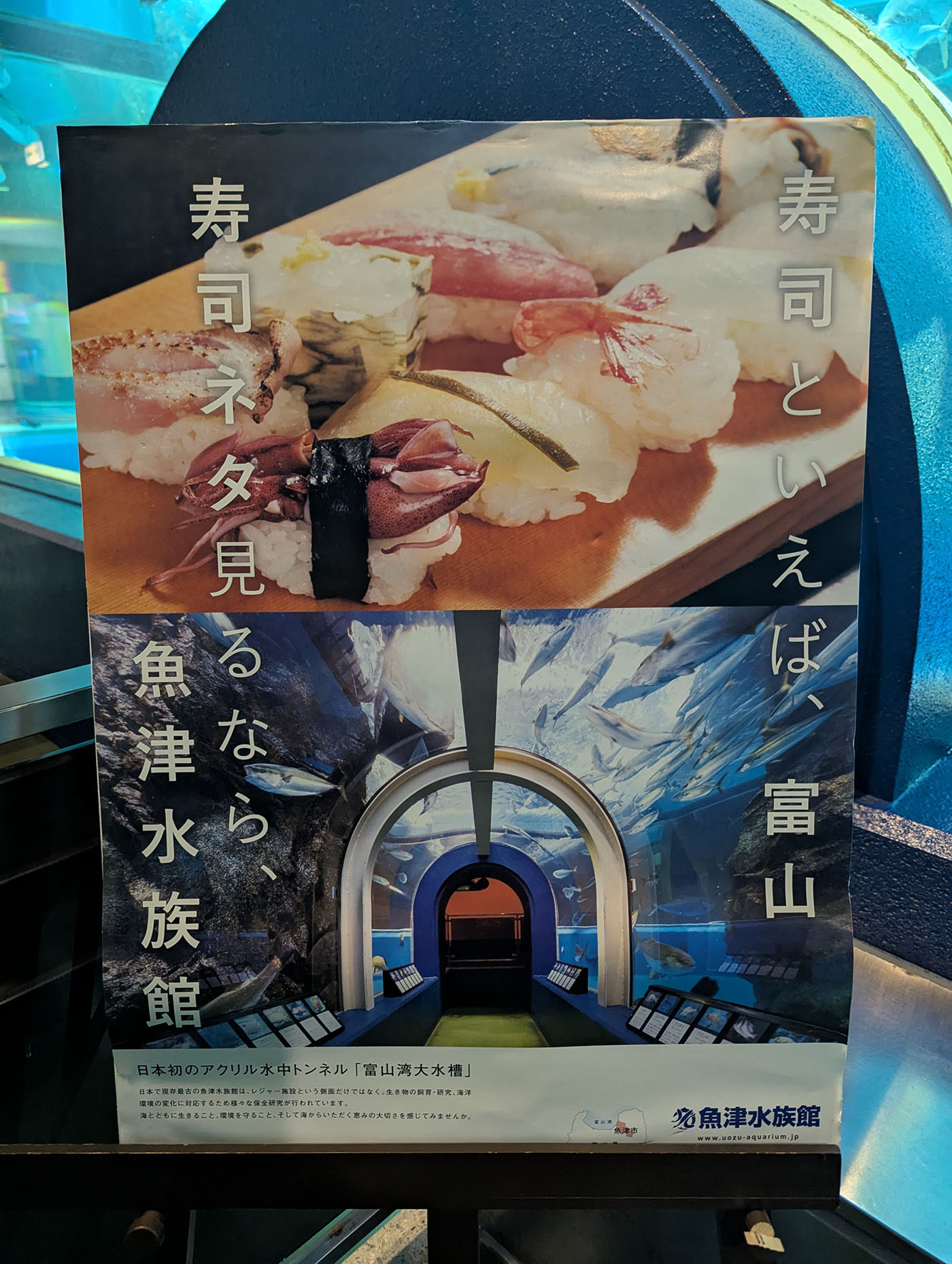 魚津水族館の「寿司ネタ見える 魚津水族館」ポスター。寿司ネタとして並ぶ富山湾の魚介類の写真と、日本初のアクリル水中トンネル「富山湾大水槽」の内部写真、立山連峰の風景写真が配置されている。
