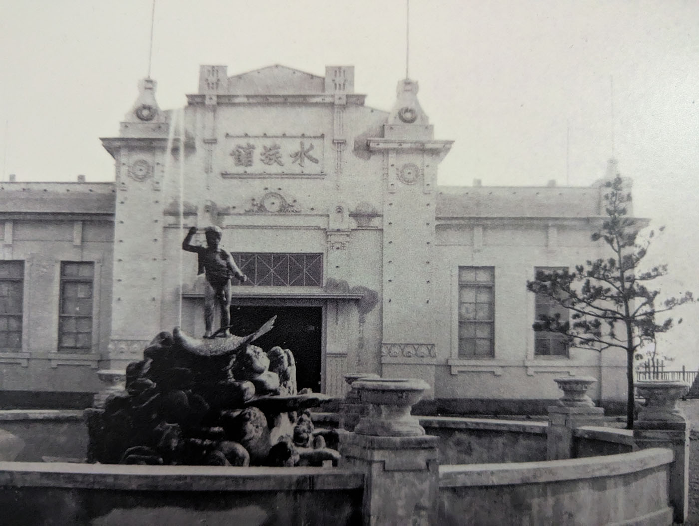 大正時代の初代魚津水族館の白黒写真。洋風建築の「水族館」と書かれた建物の前に、噴水と石造りの装飾が配置されている。左右対称の瀟洒な建物で、当時のモダンな雰囲気が感じられる。