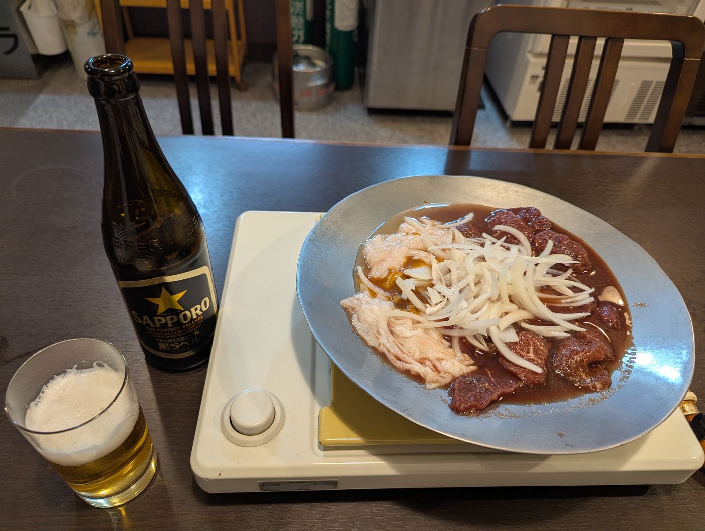 卓上コンロの鍋に入った煮込みジンギスカンと、サッポロビールの瓶とグラスが並ぶ食卓