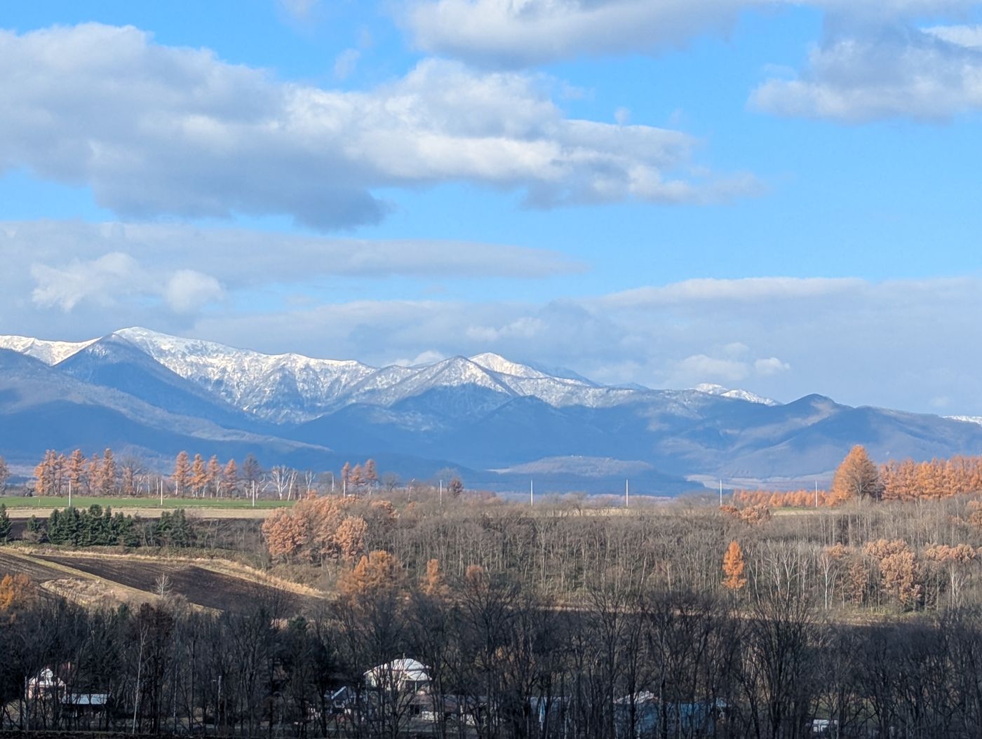 晩秋の十勝平野と、雪をまとい始めた山並みが青空の下に広がる風景