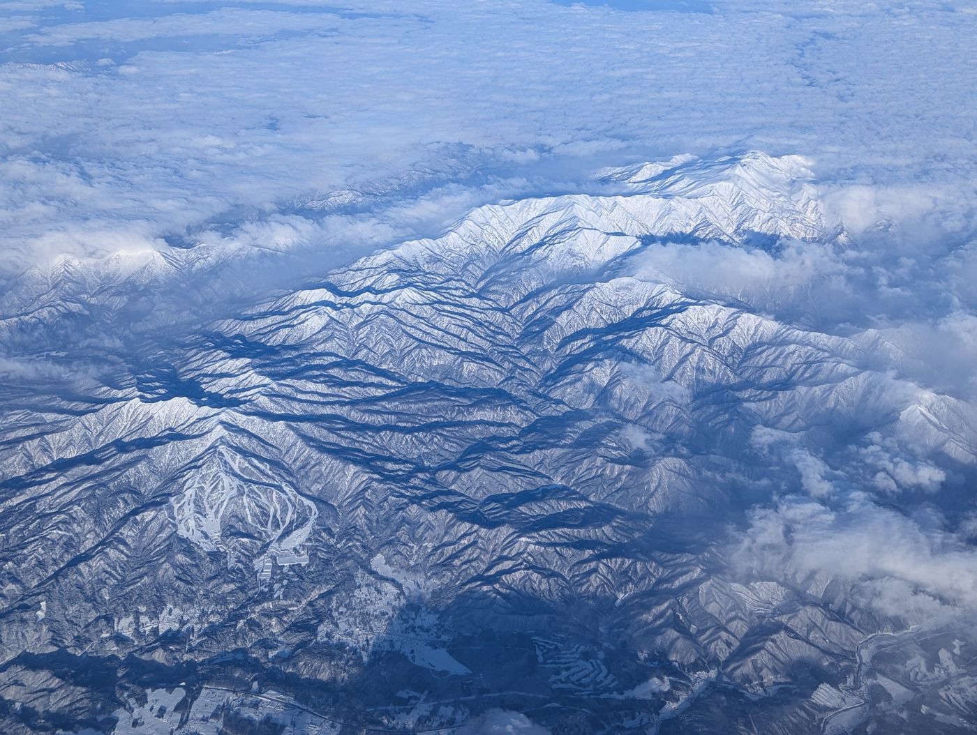 雲間から見下ろした雪に覆われた山脈と谷筋の航空写真