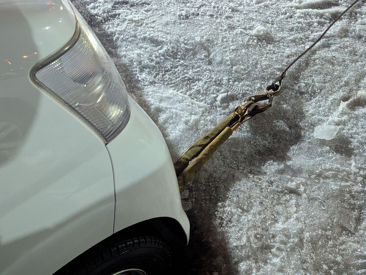 氷で動けなくなった軽バンの後部に牽引ロープが掛けられ、雪解けの路面で救出作業が分かる様子