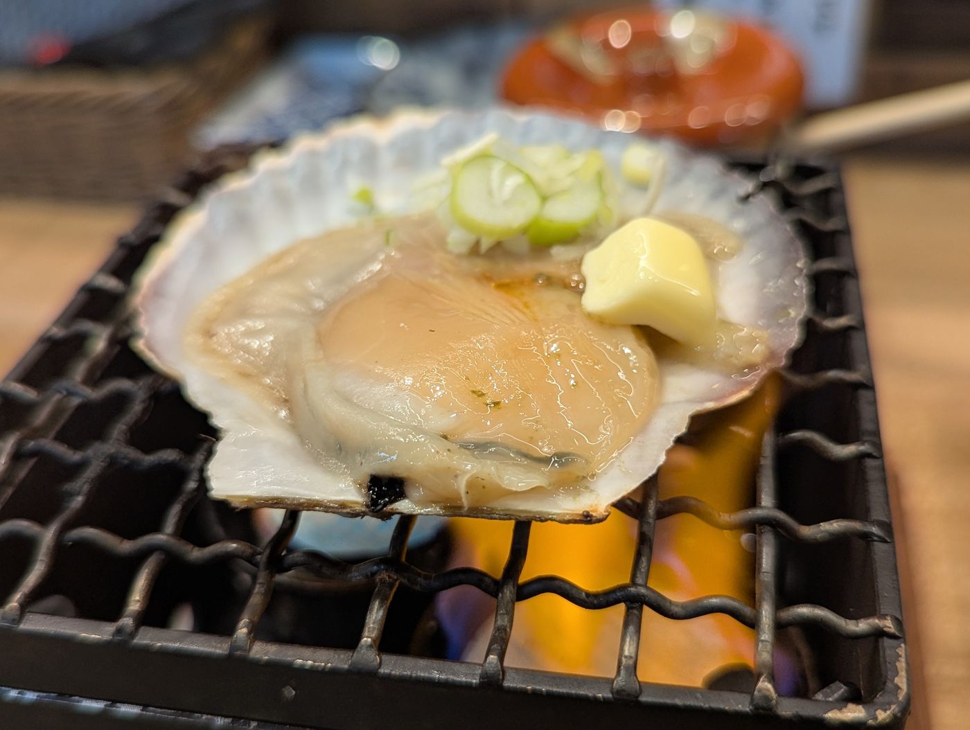 帯広駅前の炉端居酒屋で、炭火の上に置かれた殻付きホタテにバターをのせて焼いている様子