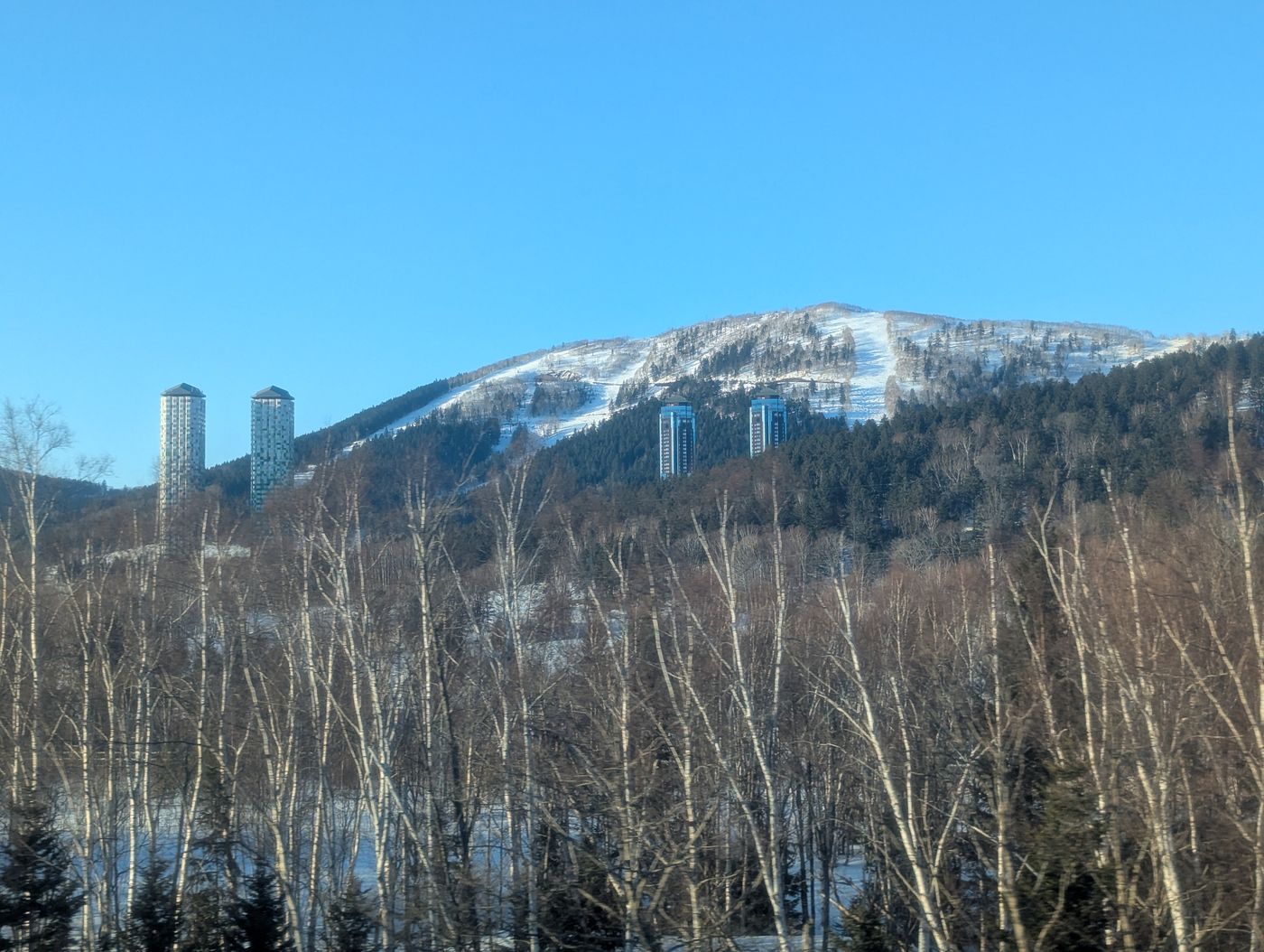 占冠付近の雪山とスキー場の斜面、青空の下に立つ高層ホテルタワー